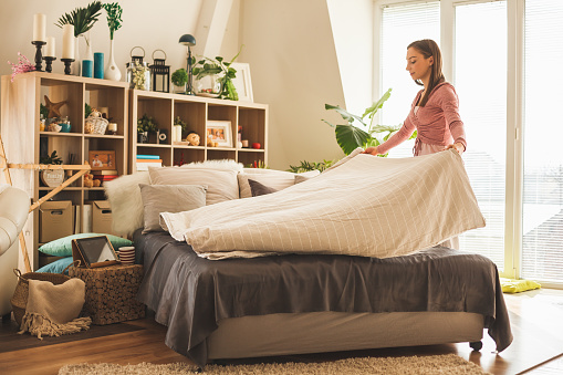 Young woman making bed in her bedroom in the morning