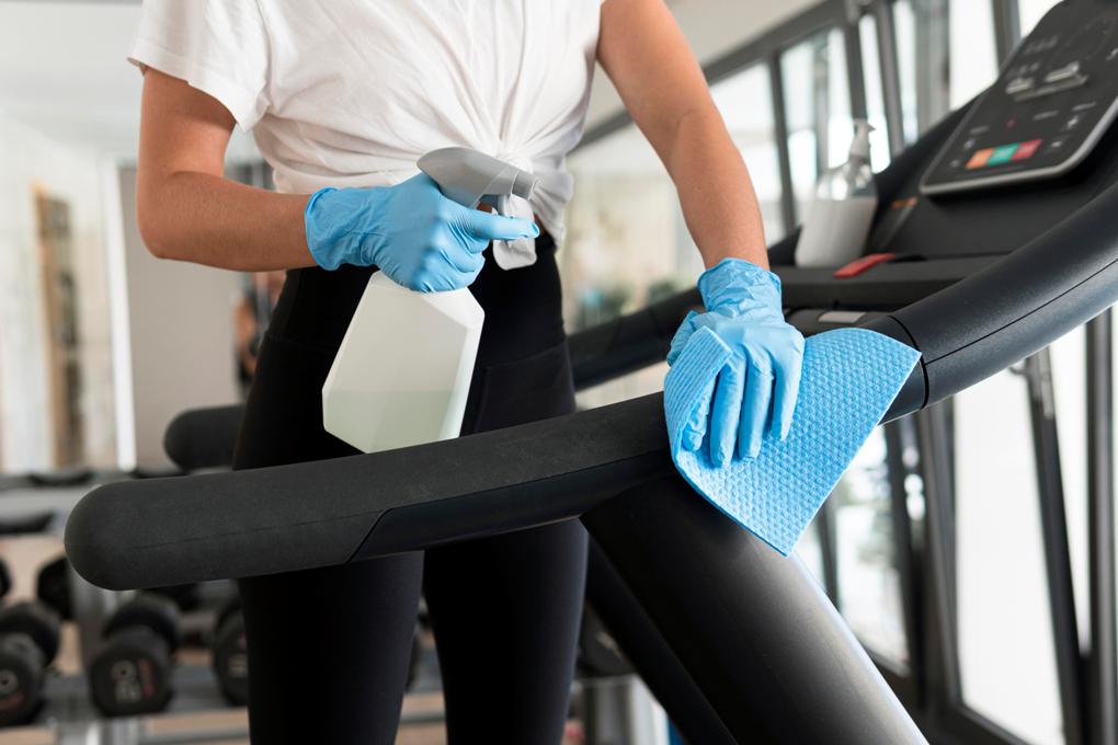 woman-with-gloves-cleaning-solution-disinfecting-gym-equipment